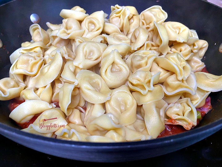 adding the tortellini to the skillet with Tuscan sauce