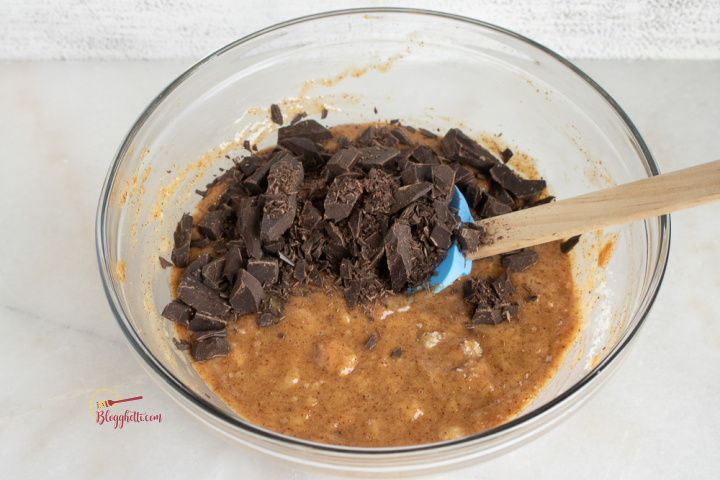 adding chocolate chunks to banana muffin batter in large bowl