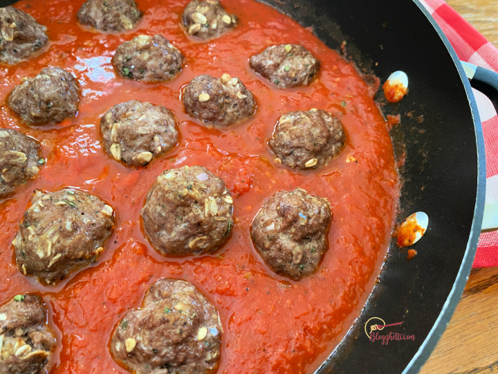 Homemade meatballs simmering in sauce for the best spaghetti and meatballs recipe.