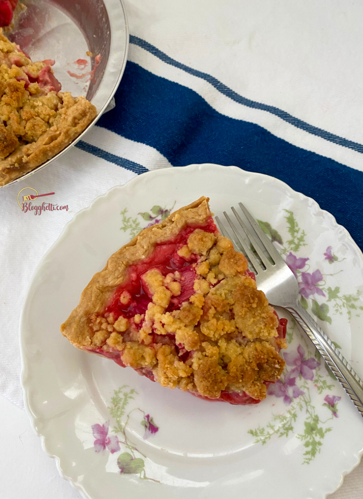 slice of strawberry rhubarb pie on flowered plate with blue towel in background