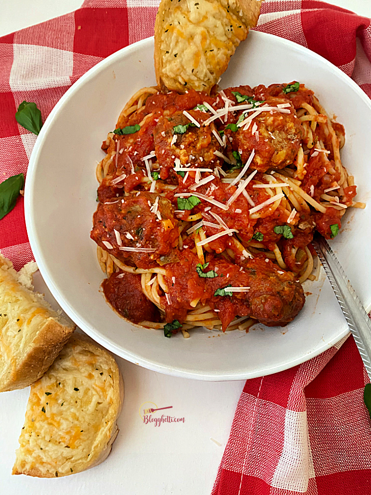 white bowl filled with spaghetti and meatballs with a side of garlic bread
