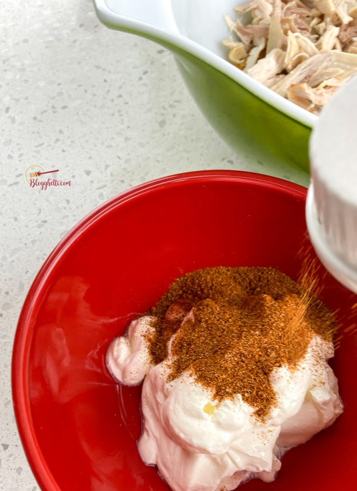 adding taco seasoning to sour cream in red bowl