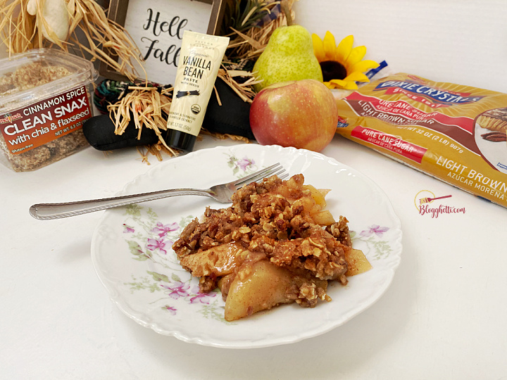 serving of apple pear crisp on white plate with some of the ingredients in the background