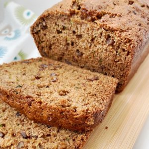 A sliced zucchini nut bread loaf on a wooden cutting board with two slices in front.