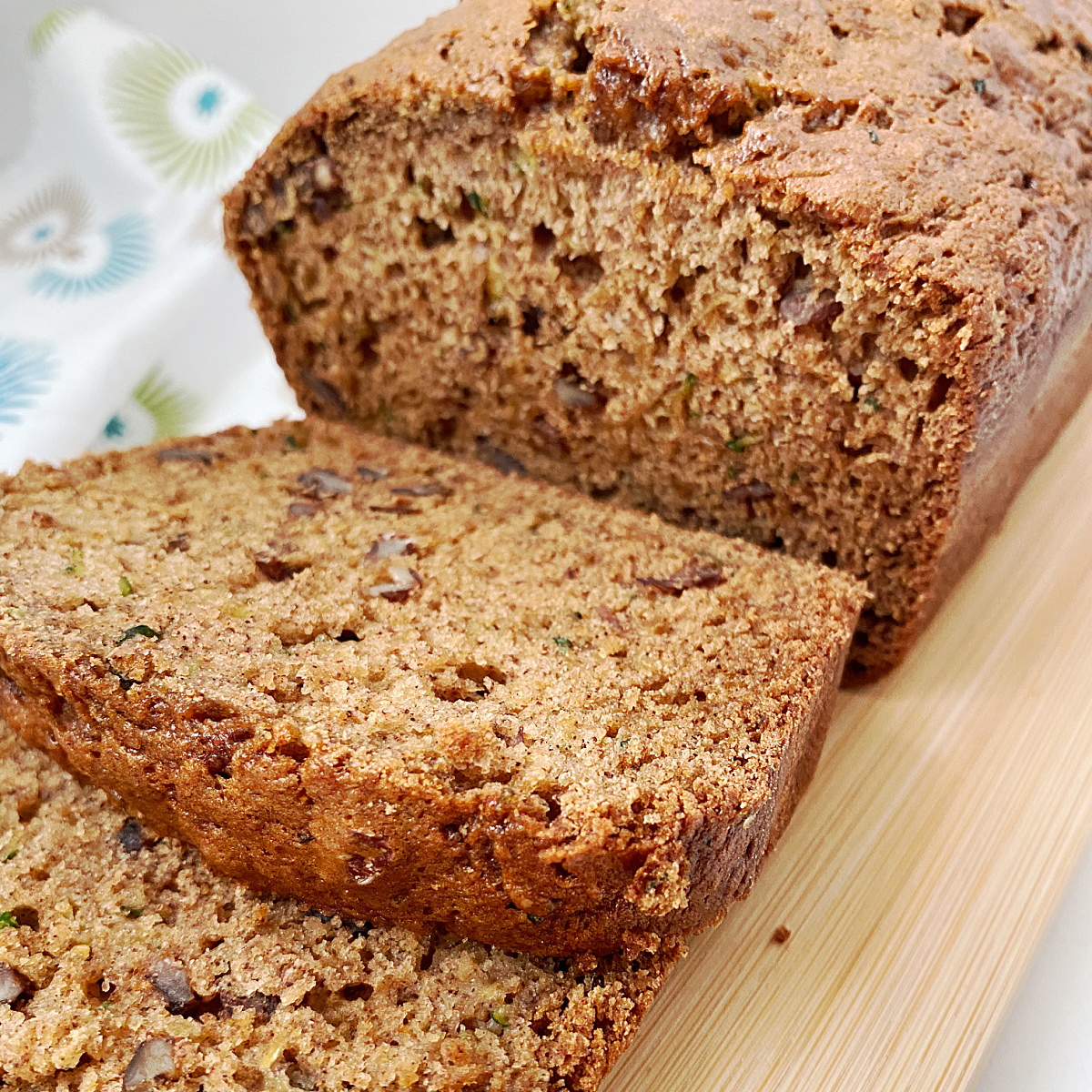 A sliced zucchini nut bread loaf on a wooden cutting board with two slices in front.