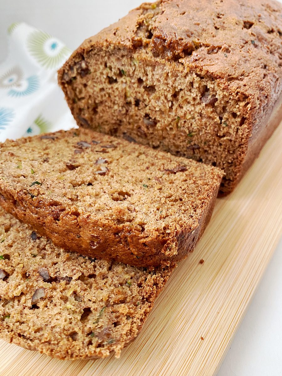 A freshly sliced quick bread loaf, revealing its moist interior and bits of zucchini, on a wooden cutting board.