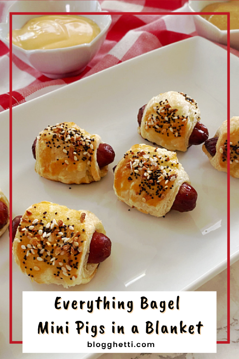 A plate of mini pigs in a blanket, wrapped in flaky pastry and topped with a delicious everything bagel seasoning. A small bowl of mustard is placed next to the plate.