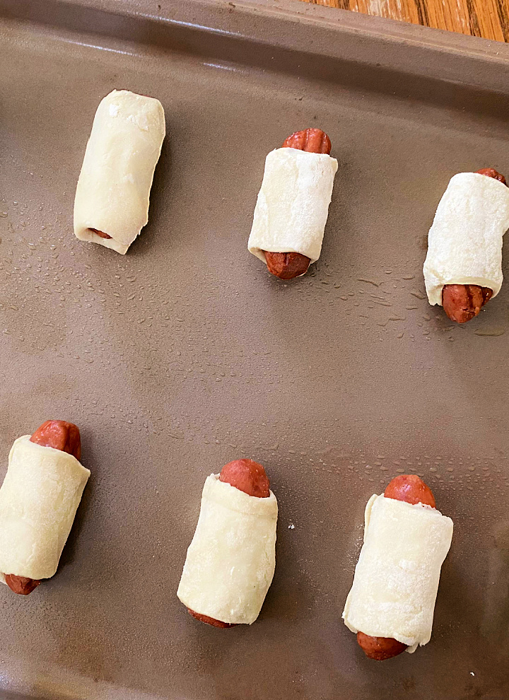 little sausages wrapped in pastry dough on baking sheet