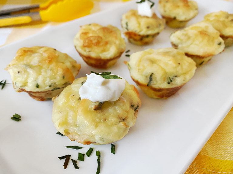 A white rectangular plate holds several baked mashed potato puffs. One in the foreground is topped with a dol
