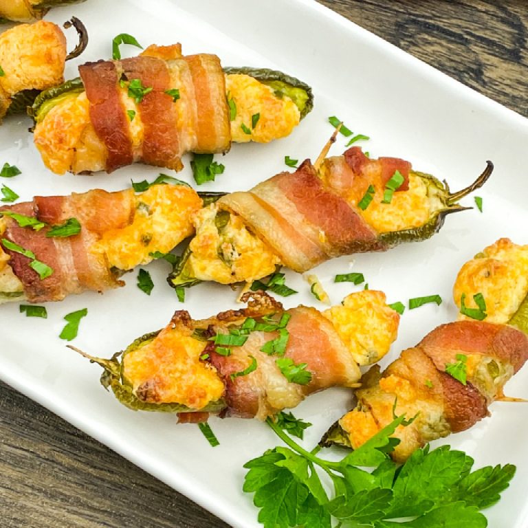 Crispy bacon-wrapped jalapeno poppers filled with a creamy cheese mixture, served on a white plate with fresh parsley.