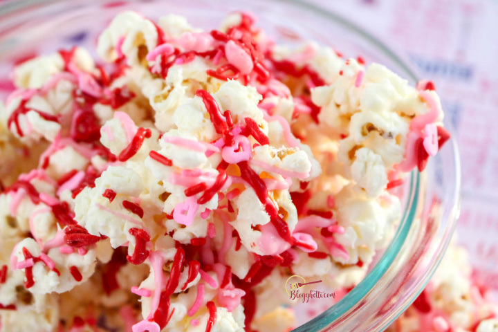 white chocolate drizzled popcorn with sprinkles in clear bowl - close up