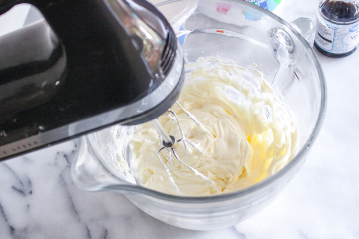 beating cream cheese with mixer in bowl