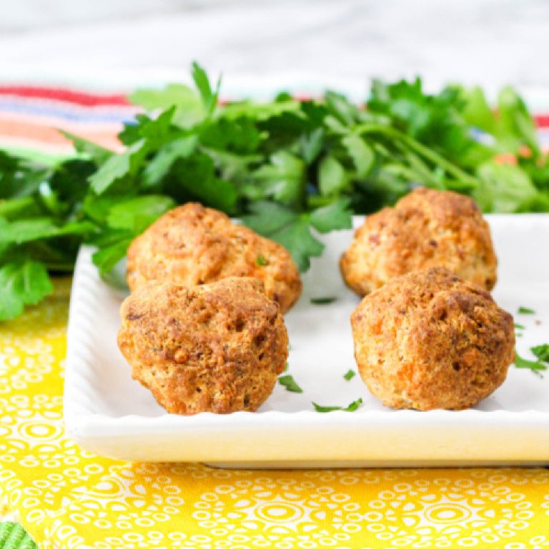 Crispy air fryer sausage balls on a white plate, garnished with fresh parsley.