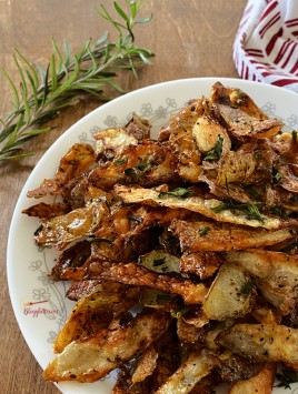 rosemary roasted potato peels on white plate with sprig of rosemary in background