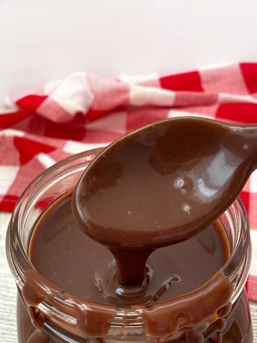 A large spoonful of thick, decadent cocoa topping being lifted out of a glass container.