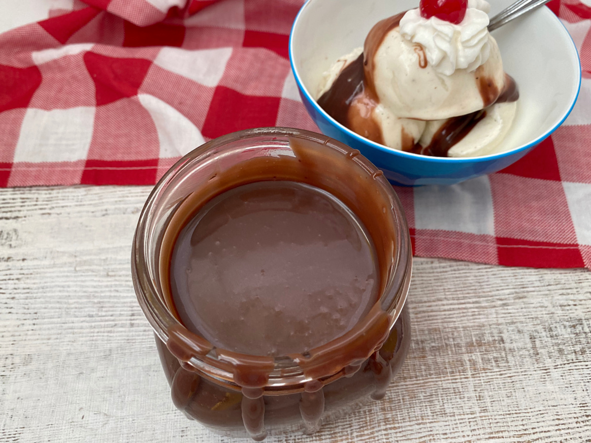 Homemade chocolate ice cream topping in a clear jar with a red and white gingham napkin.