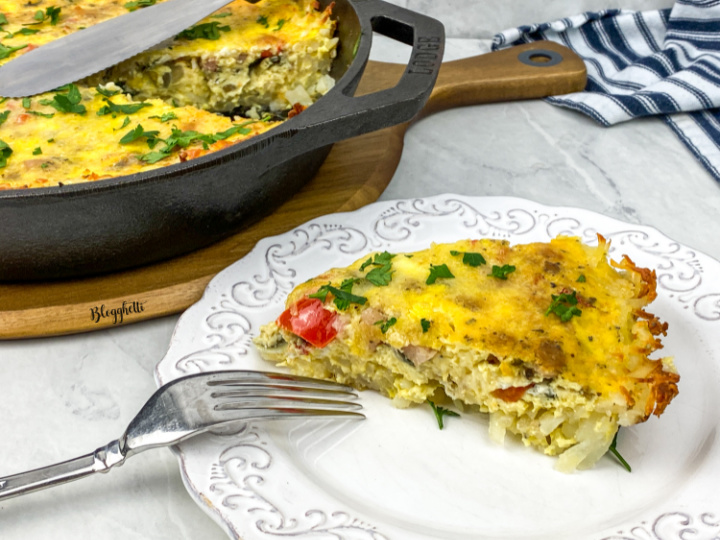 slice of vegetable frittata with potato crust on a white plate with fork