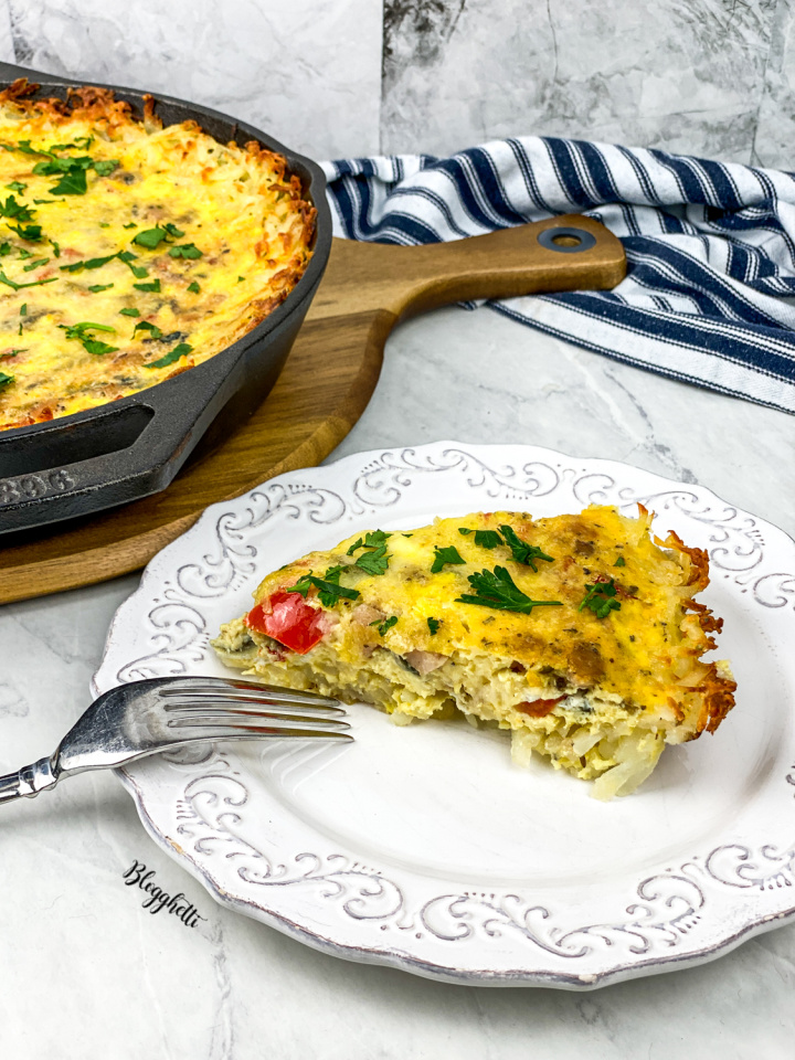 vegetable filled frittata on white place with cast iron skillet in background