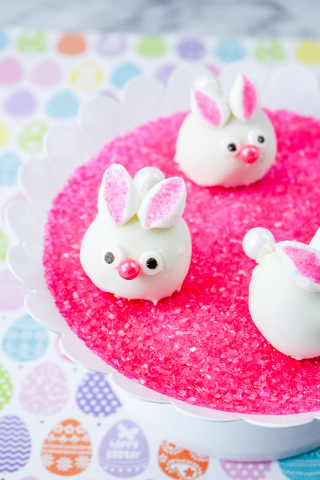 bunny face oreo balls sitting on pink sugar crystals on a cake plate