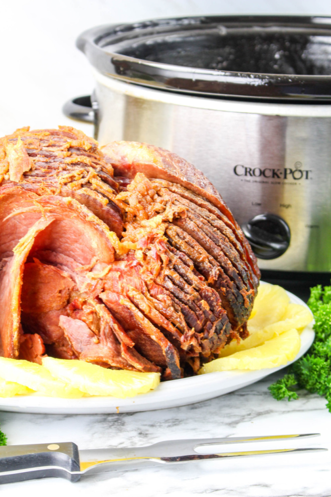 picture of spiral ham slices on white plate with slow cooker in background
