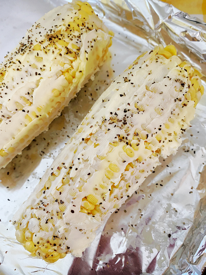 adding salt and pepper to buttered corn to roast