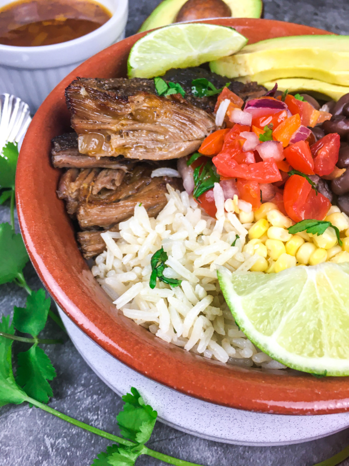bowl filled with delicious pork carnitas, rice, and garnishes