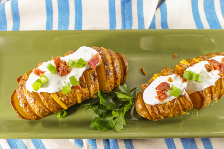 two hasselback potatoes loaded with toppings on serving platter