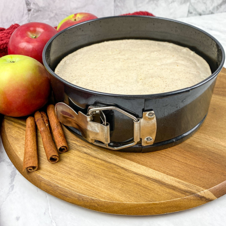 apple cinnamon cheesecake in pan on round wooden cutting board