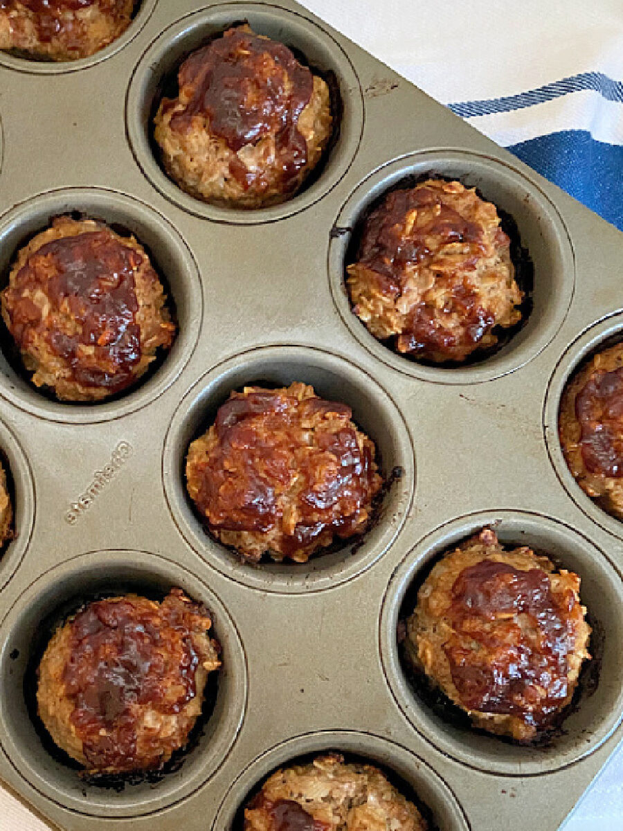 Overhead view of baked Mini Turkey Meatloaves topped with BBQ sauce in a metal muffin tin.