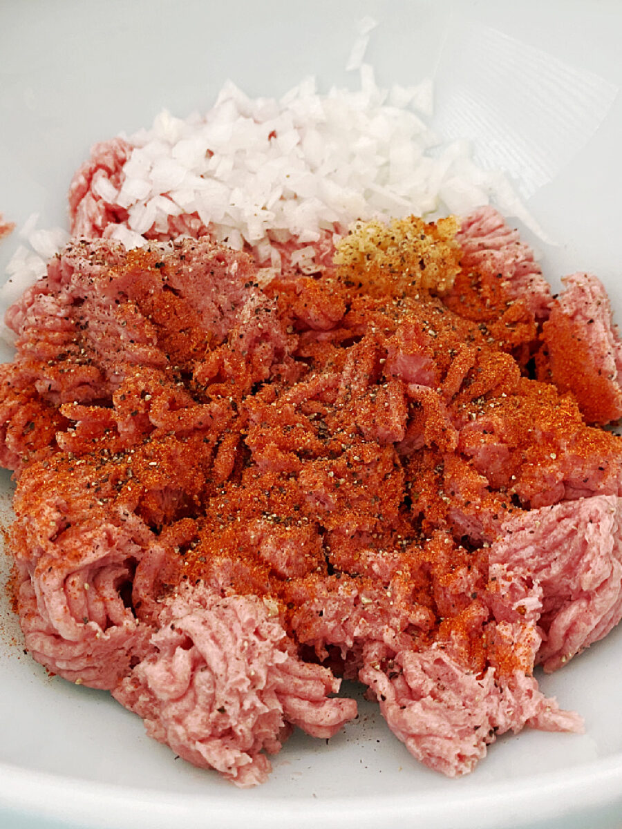 Raw ground turkey topped with diced onion and seasonings in a white mixing bowl.