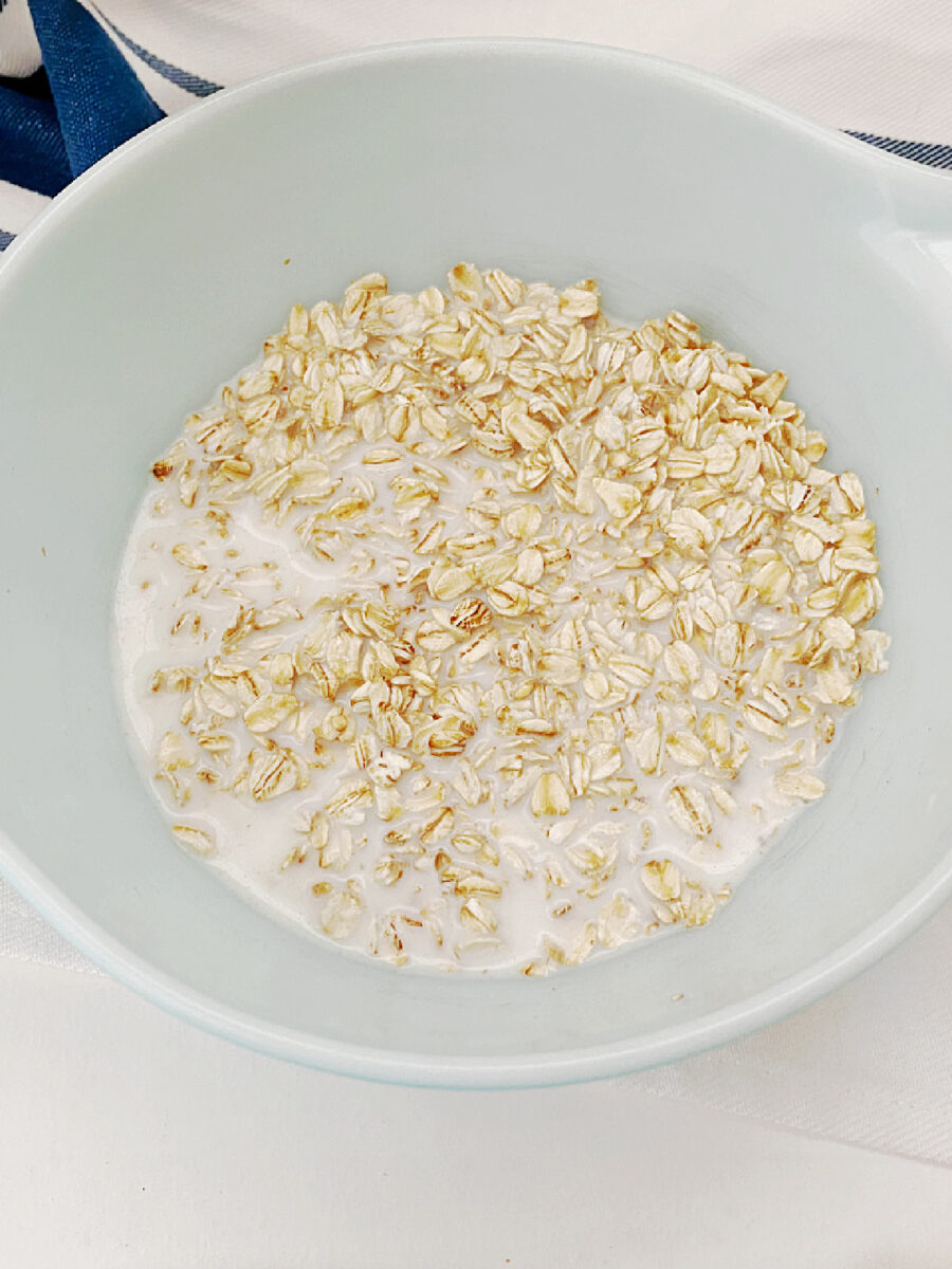 Rolled oats soaking in milk in a white bowl before being added to Mini Turkey Meatloaves.