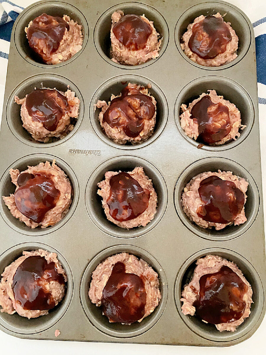 Unbaked Mini Turkey Meatloaves topped with BBQ sauce arranged in a muffin tin before baking.