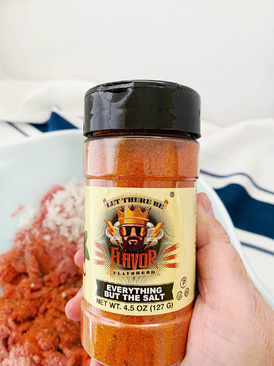 Hand holding a bottle of Flavor God Everything But the Salt seasoning in front of the turkey meatloaf ingredients.