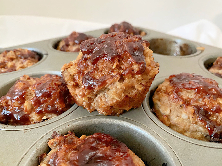 Single Mini Turkey Meatloaf lifted from a muffin tin with BBQ glazed meatloaves surrounding it.