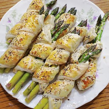 baked puff pastry wrapped asparagus on white plate