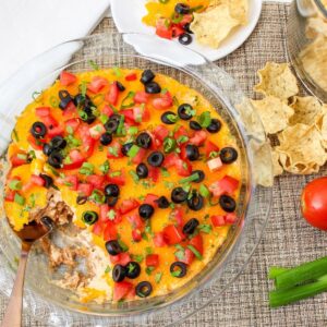 Hot taco dip baked in a glass pie dish with melted cheddar cheese, fresh toppings, and a serving spoon ready for scooping.