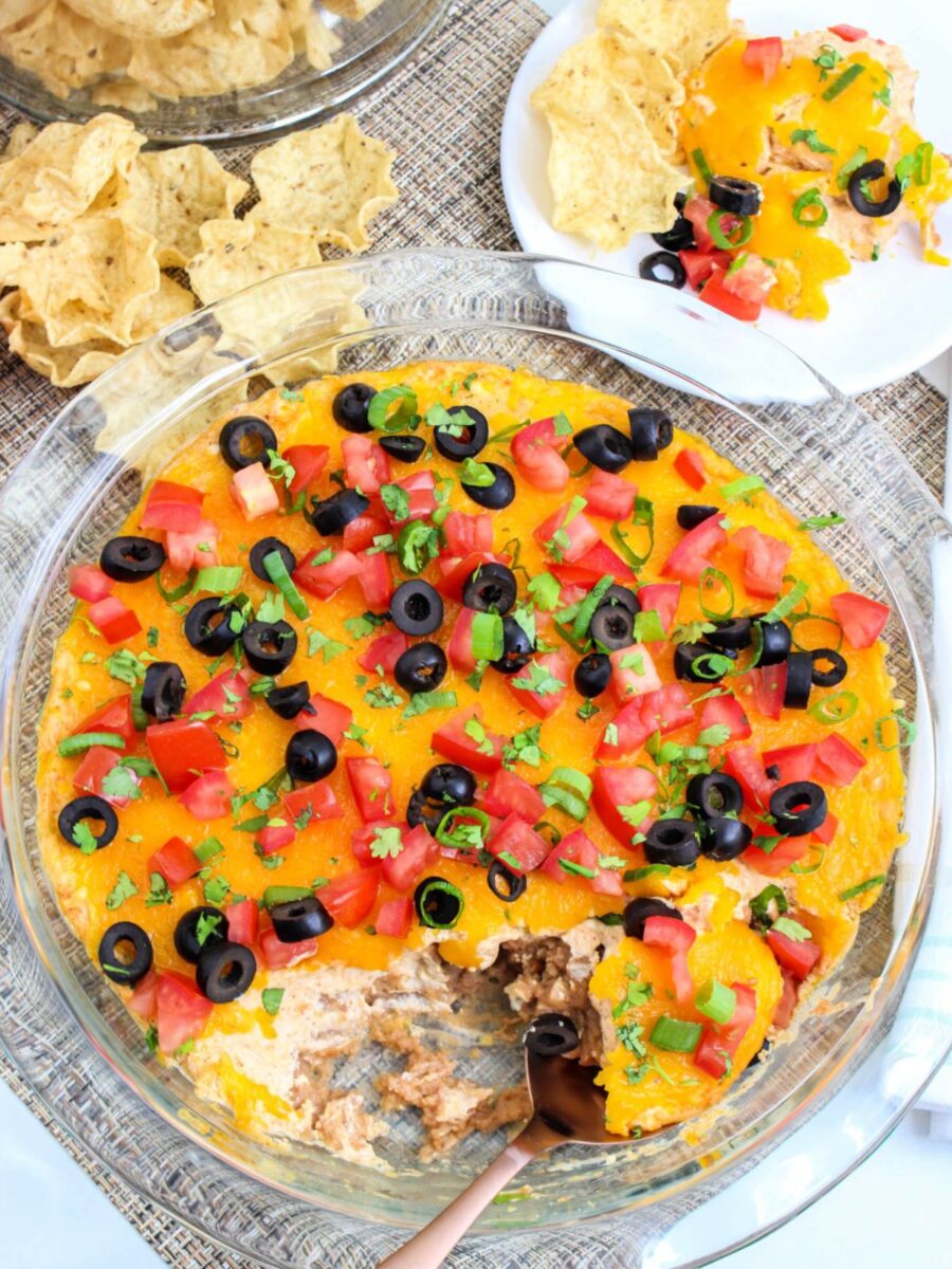 Overhead view of a warm taco dip served in a glass baking dish with tortilla chips ready for dipping.