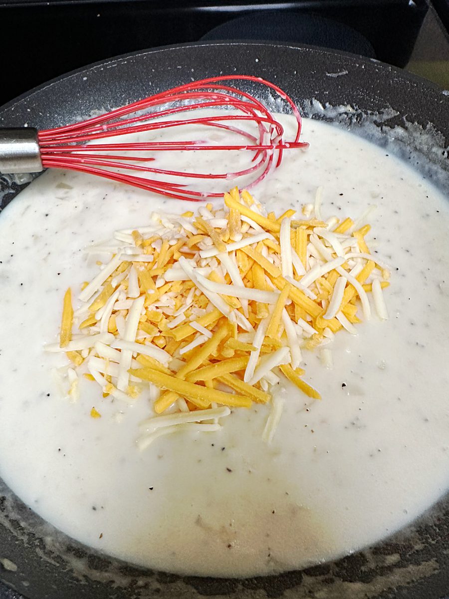 adding cheese to the white sauce in skillet