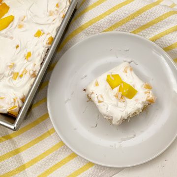 overhead shot of slice of mango coconut cake on white plate and yellow towel
