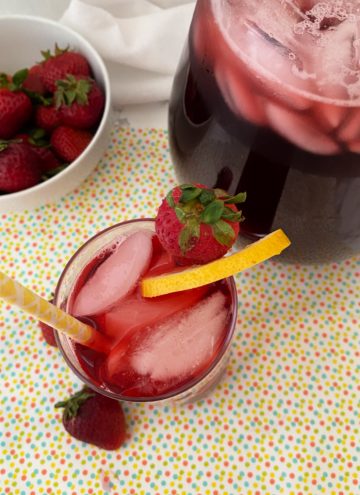 pitcher of hibiscus iced tea with strawberries and a glassful of tea and ice