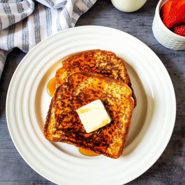 Cinnamon French toast slices with butter and syrup on white plate