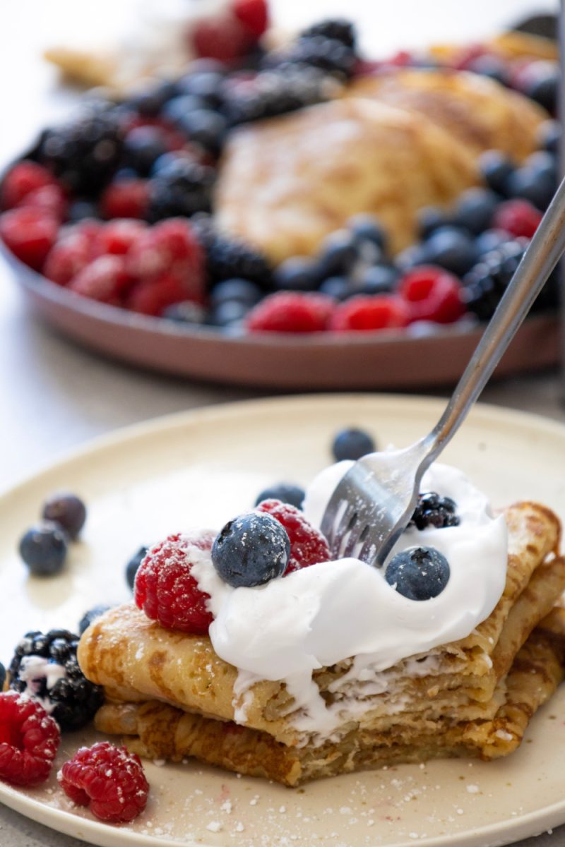 serving of crepes and berries with cream on white plate