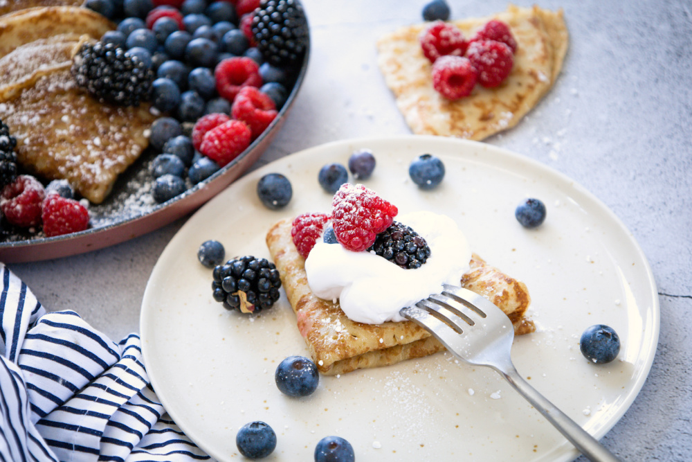 white plate with a crepe, berries and whipped cream
