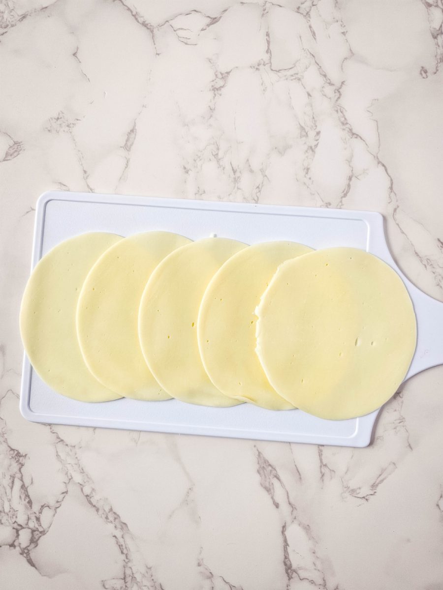overlap provolone cheese slices on cutting board