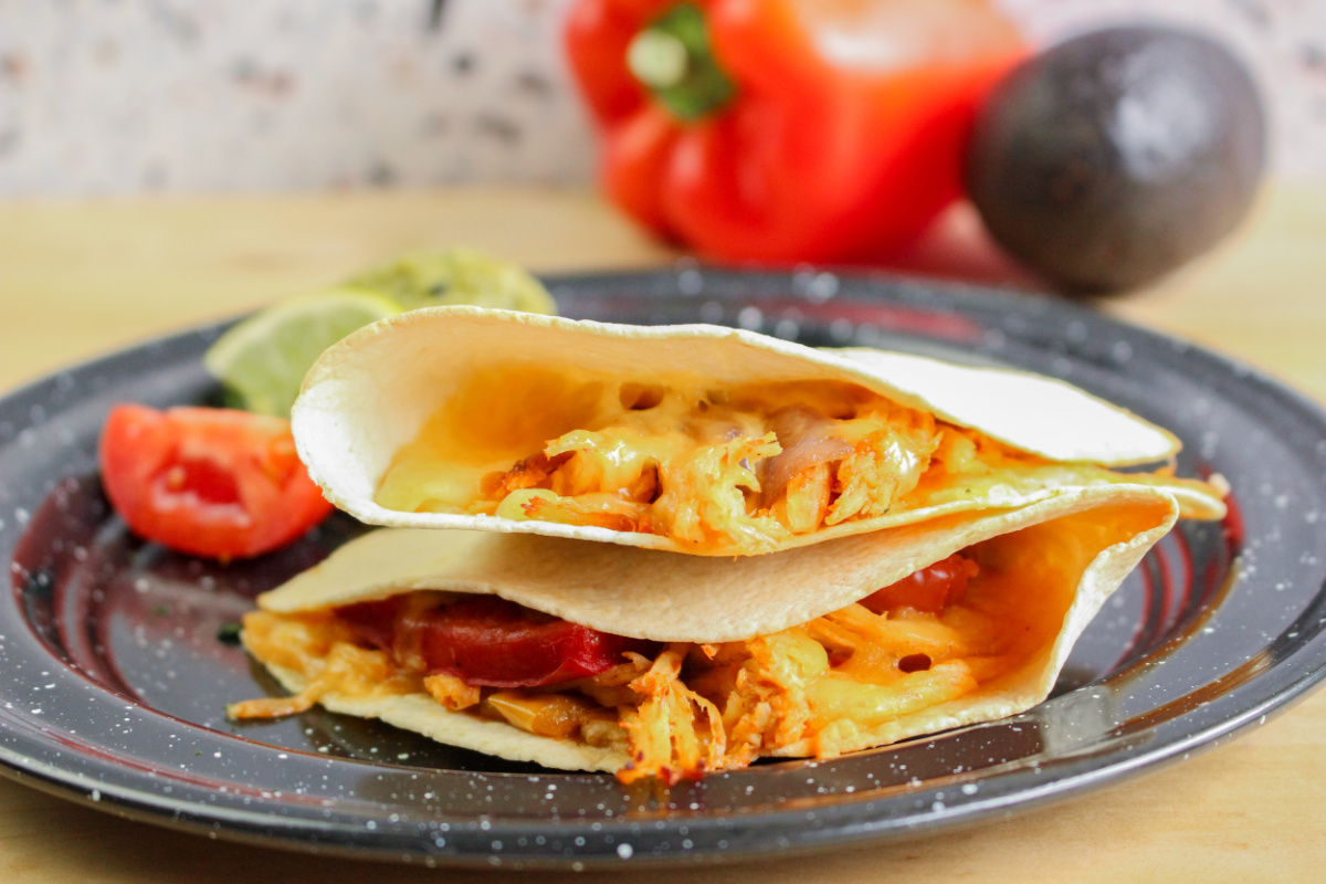 Two golden-brown quesadillas stacked on a black plate, filled with melted cheese, shredded chicken, and vegetables.