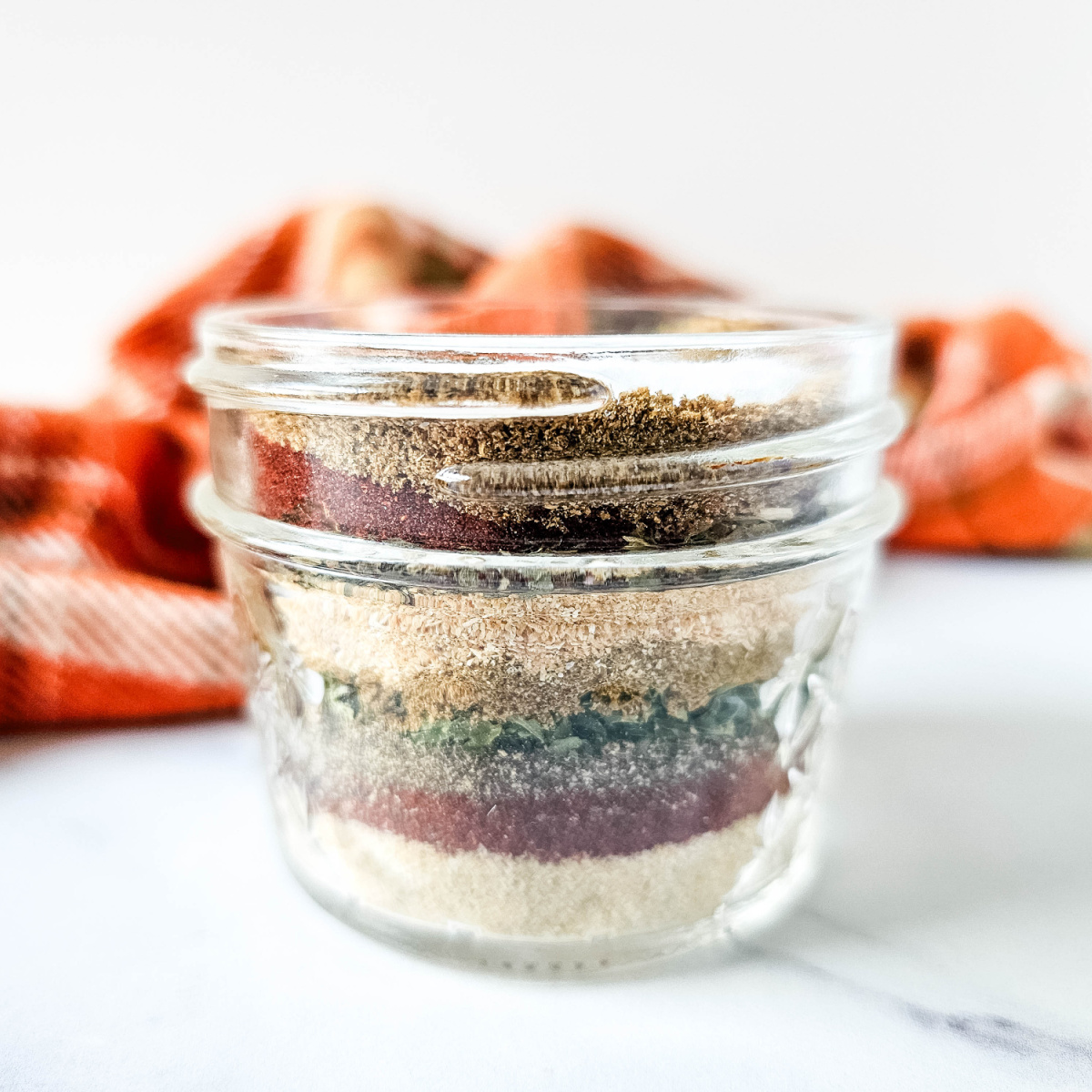 A mason jar filled with layered spices and herbs, creating a colorful and flavorful seasoning blend. The seasoning is a copycat recipe for Flavor God's Everything Seasoning.