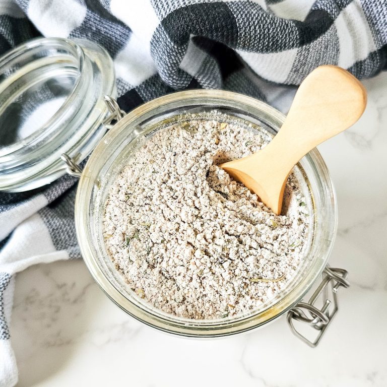 Alt text: A close-up of a glass jar filled with homemade beef stew seasoning. A small wooden spoon rests in the jar, scooping out some of the seasoning.