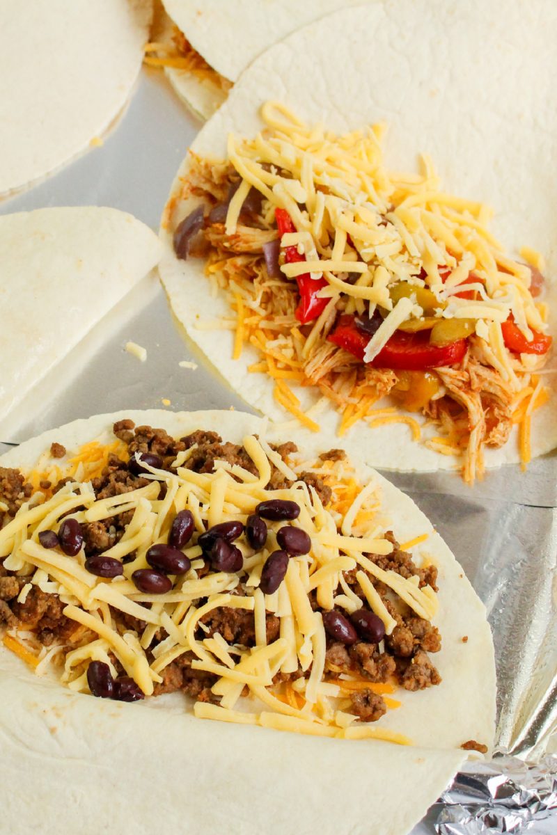 Two large flour tortillas filled with different ingredients. The left tortilla is topped with seasoned ground beef, black beans, and shredded cheese. The right tortilla is filled with shredded chicken, peppers, onions, and cheese.