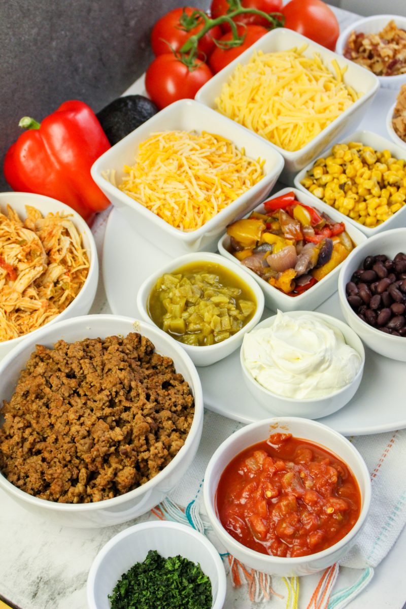 view of a variety of ingredients for making tacos or quesadillas, including shredded chicken, ground beef, black beans, corn, peppers, onions, tomatoes, shredded cheese, sour cream, salsa, and cilantro.