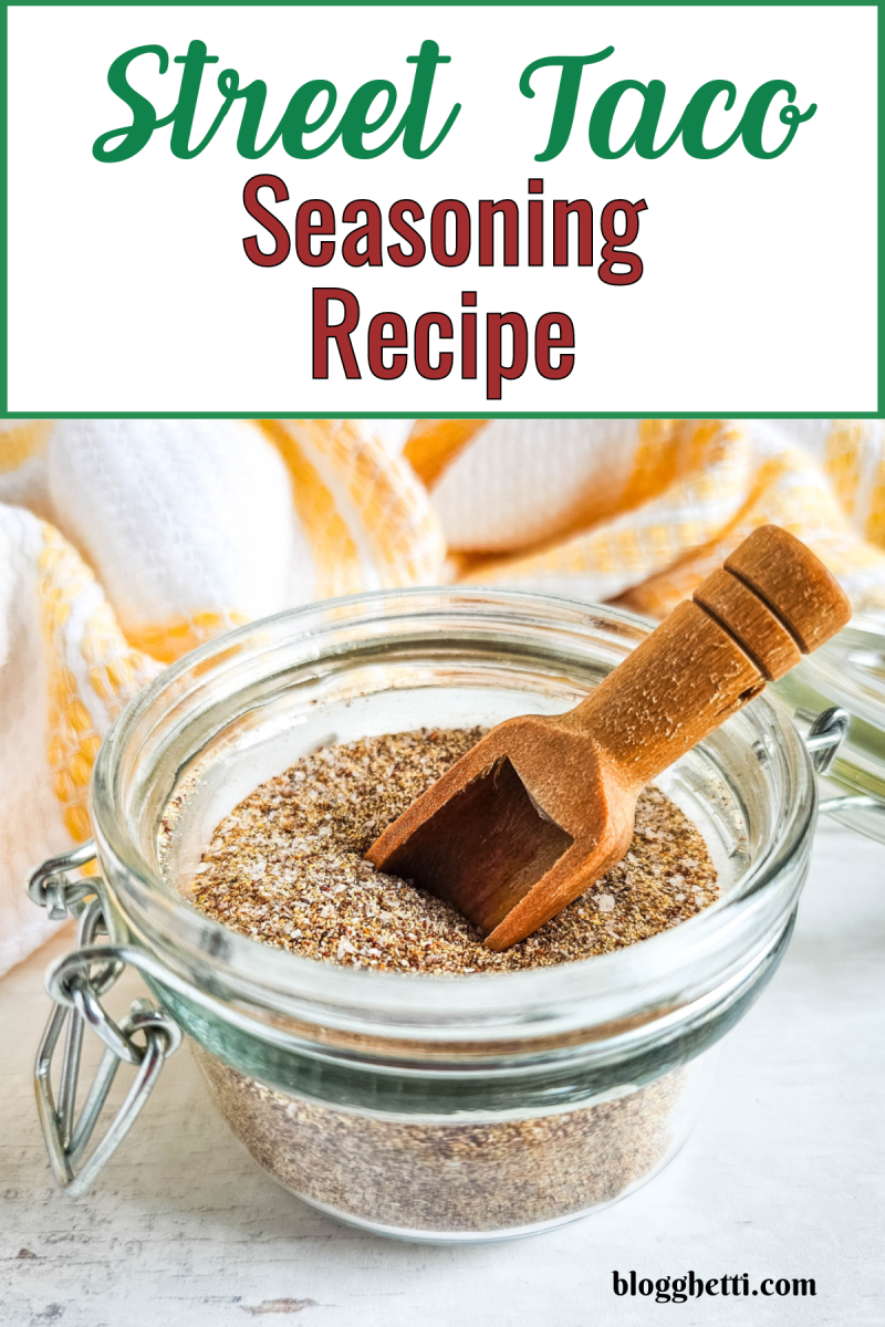 A glass jar filled with a brown spice blend, with a small wooden scoop dipping into it. A yellow and white striped towel is blurred in the background. The title "Street Taco Seasoning Recipe" is written in bold above the image.